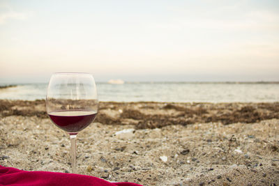 Close-up of wineglass on beach against sky during sunset