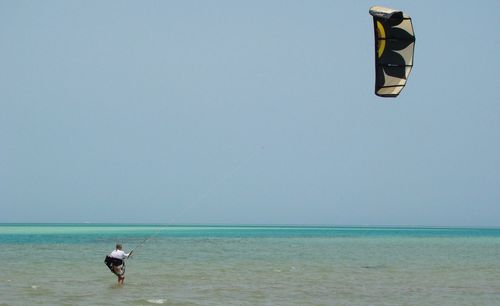 Man kiteboarding on sea against clear sky