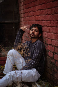 Portrait of young man sitting against brick wall