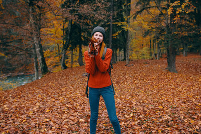 Full length of young woman standing by tree during autumn