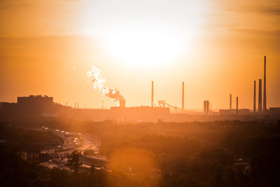 Smoke emitting from factory against sky during sunset