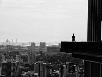 Man standing in balcony over cityscape against sky