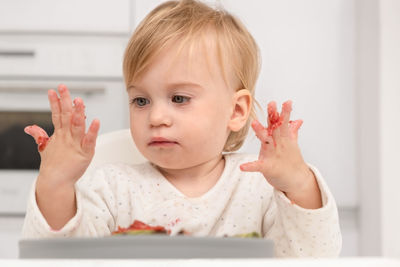 Closeup of caucasian baby eating at kitchen looking at dirty hands 