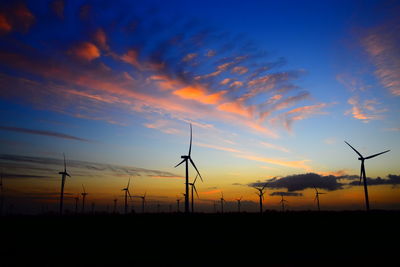 Silhouette wind turbines on field against sky during sunset