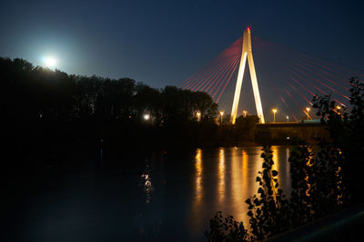 Illuminated bridge over river against sky at night