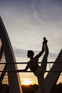 Silhouette man standing by railing against sky during sunset