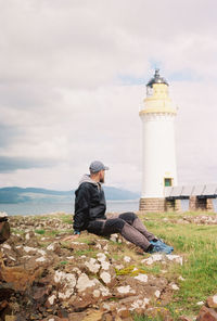 Man sitting on lighthouse against sky