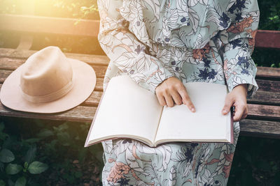 Midsection of woman reading book while sitting on bench