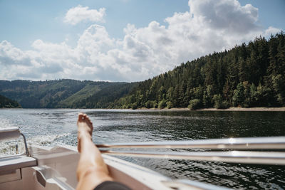 Midsection of person by lake against sky