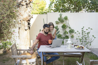 Man using laptop with woman standing behind in back yard