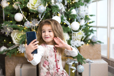 Portrait of girl holding mobile phone at christmas tree