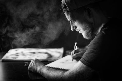 Side view of man making drawing on paper against black background