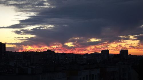 Silhouette cityscape against dramatic sky during sunset