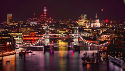 Illuminated bridge over river in city at night