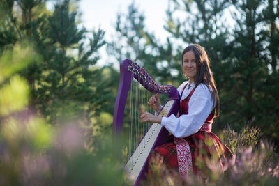 Portrait of woman playing harp against trees in forest