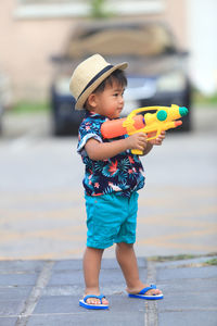 Cute boy holding toy gun standing outdoors