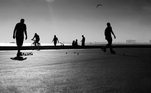 Silhouette people skateboarding on road against sky