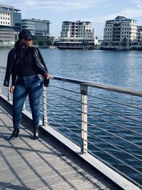 Full length of woman standing by railing against river in city