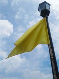 Low angle view of yellow flag against cloudy sky