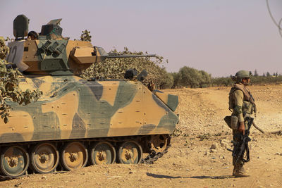 Full length of soldier standing by tank on battlefield