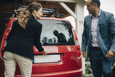 Businessman opening car trunk while looking at man