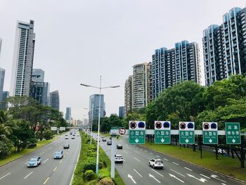 Vehicles on road by buildings in city against sky