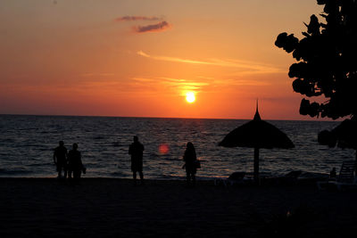 Silhouette people on beach against sky during sunset