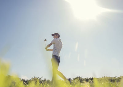 Teenage boy playing golf against clear sky during sunny day