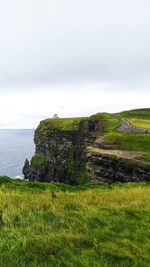 Scenic view of grassy field by sea against sky