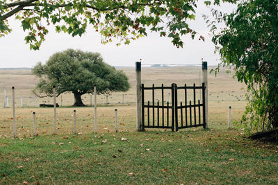 Wooden gate on field by trees against sky