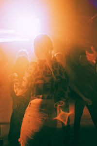 Back lit young woman dancing at illuminated nightclub