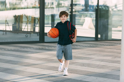 A cheerful boy with a backpack and a basketball. a boy hurries to basketball practice. 