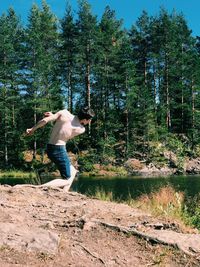 Shirtless young man skimming stones in lake a forest