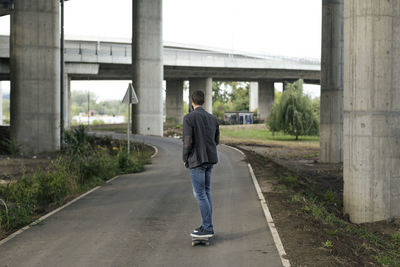 Man skateboarding on road against bridge in city
