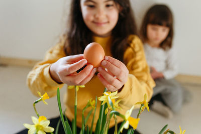 Sitting girl in yellow top holding egg in hands while smaller girl sits behind