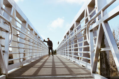 Full length of man standing on footbridge against sky