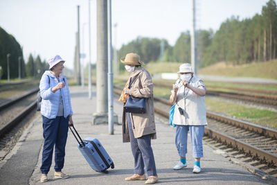 Three old senior women on  platform waiting for the train and wearing a face mask during a pandemic