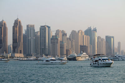 Sailboats in city by sea against clear sky