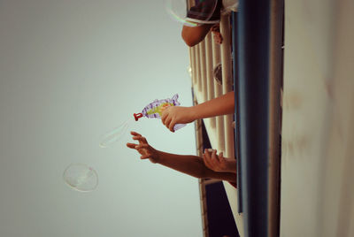 Cropped image of children playing with squirt gun against sky