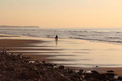 Silhouette man standing on beach against clear sky during sunset