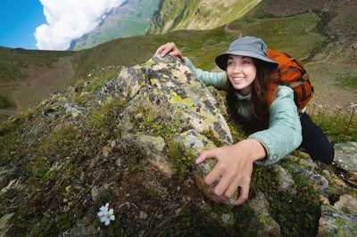 Young tourist woman smiles and climbs to the top of the cliff with a backpack. climbing a steep