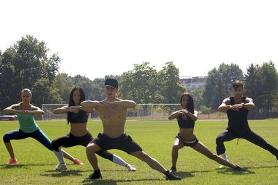 Full length portrait of people exercising on field against sky