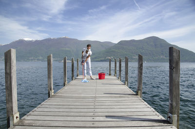 Woman cleaning pier over lake against mountains