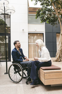 Full length senior businesswoman sitting and enjoying with physically disabled colleague at networking event in conventi