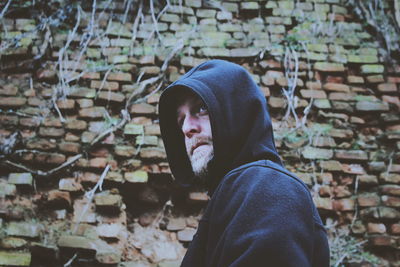 Man in hood- clothing standing against brick wall
