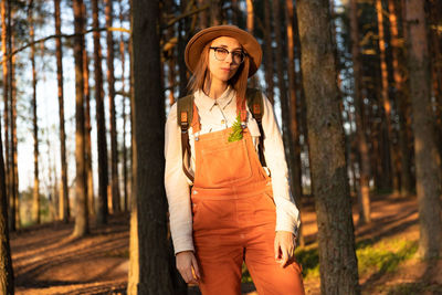 Portrait of woman standing by tree trunk in forest