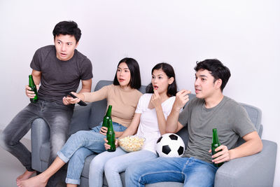 Shocked friends having popcorn and drink while sitting on sofa at home