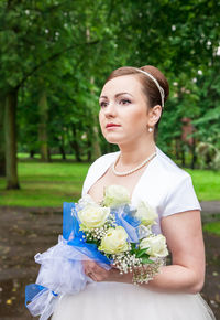 Bride holding bouquet while standing against trees