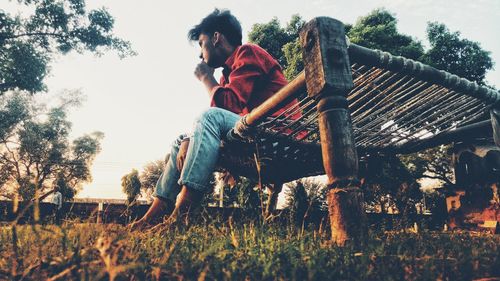 Low angle view of men sitting on wooden structure against sky