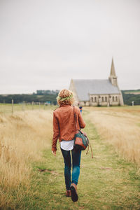 Rear view of woman walking on field against sky